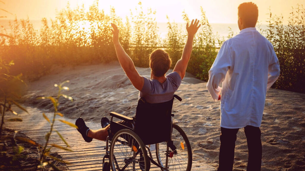 Man in wheelchair enjoying sunrise beach with his nurse